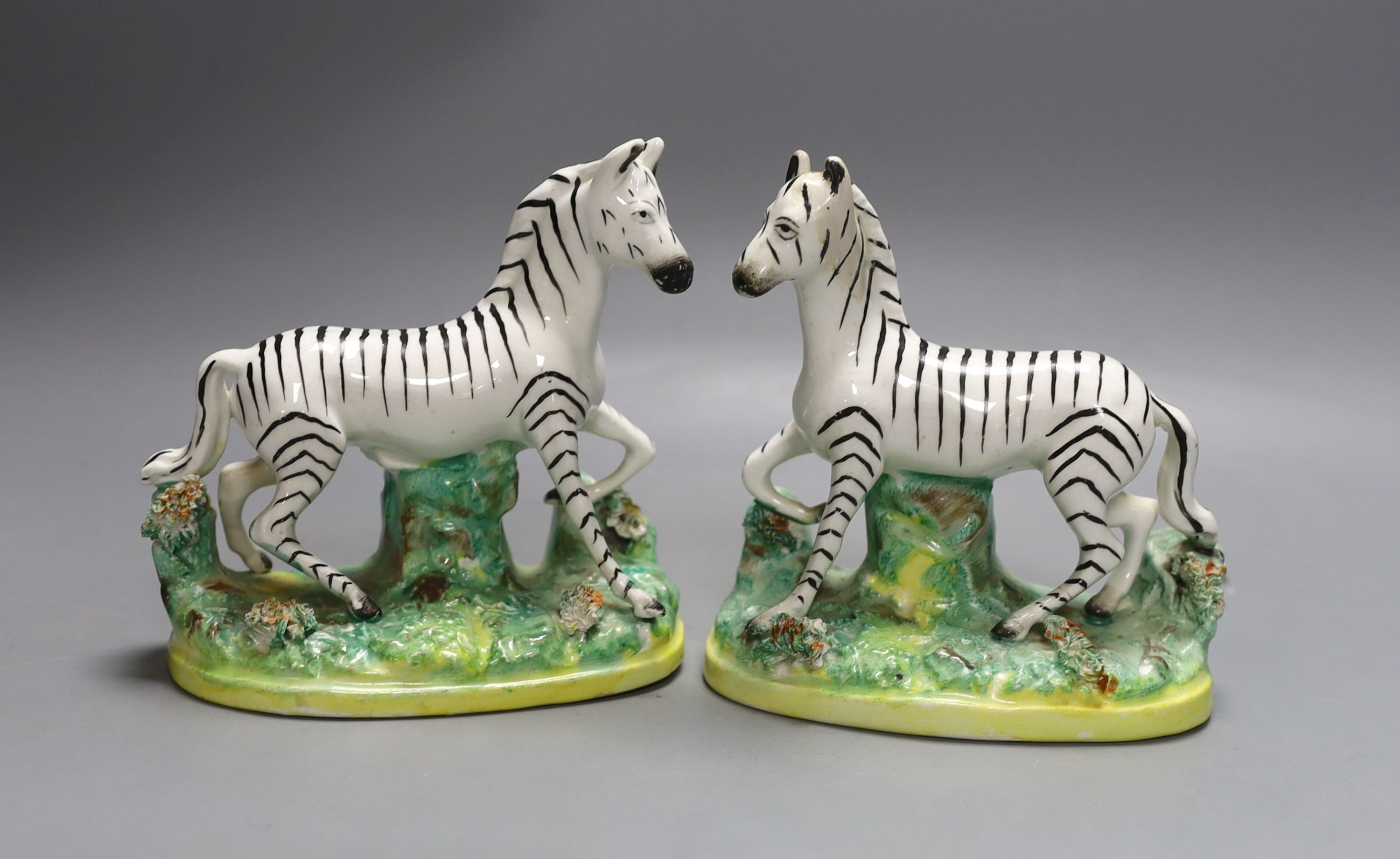 A pair of Victorian Staffordshire models of zebra, standing on an oval tree stump bases 12cm long